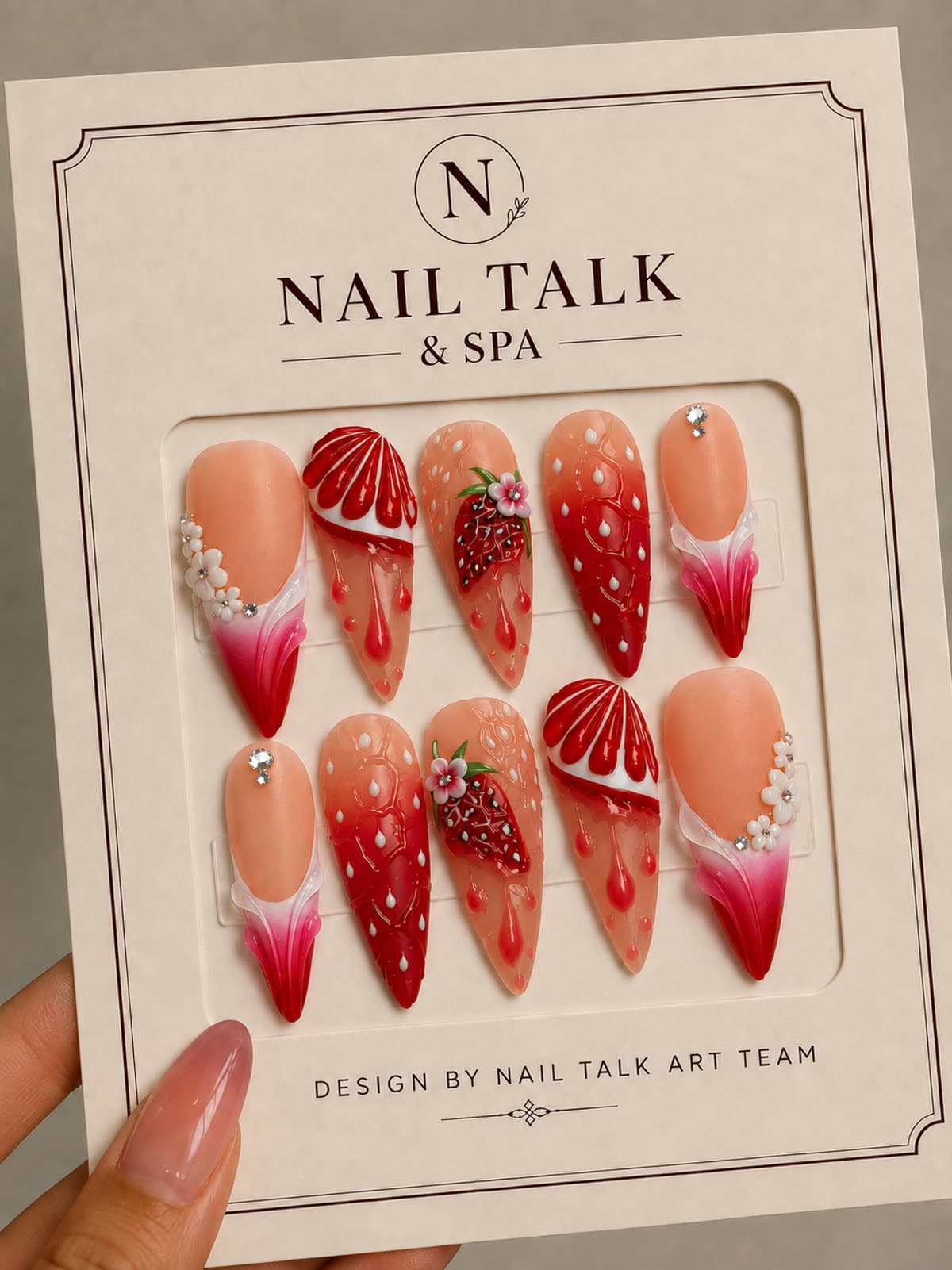 A handmade press-on nail set with strawberry nail art, held up on its Nail Talk & Spa packaging card